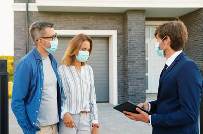 estate agent with man and woman outside of a house all wearing face masks